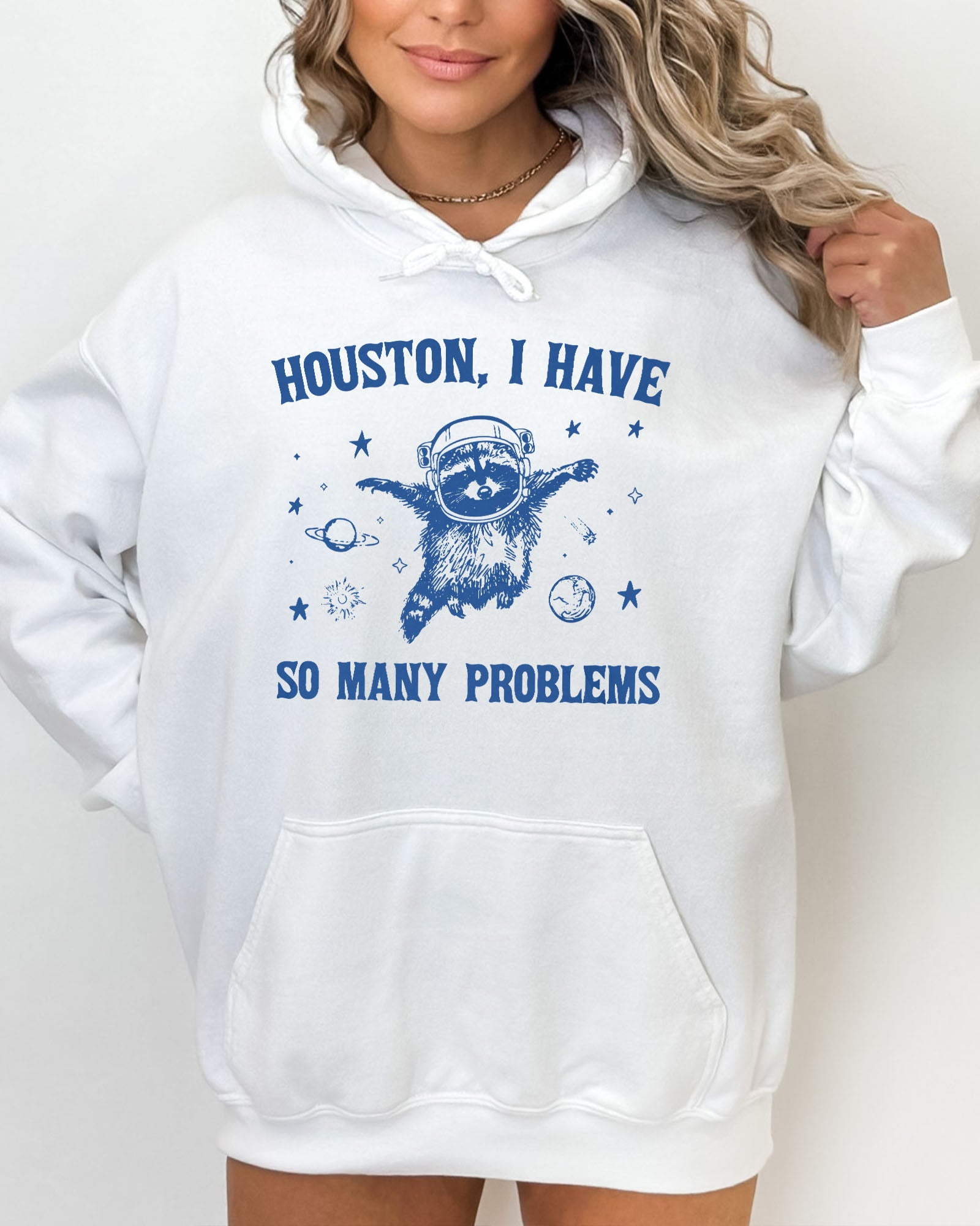 Woman wearing a white hoodie featuring a funny retro-style astronaut raccoon space graphic and the quote 'Houston I Have So Many Problems'.