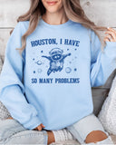 Woman wearing a light blue sweatshirt featuring a funny retro astronaut raccoon graphic and the quote 'Houston I Have So Many Problems'.