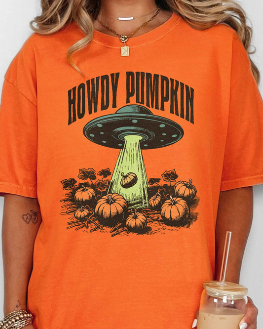 Close up of woman wearing a burnt orange "Howdy Pumpkin" shirt with a retro graphic of a UFO abducting pumpkins from a field.