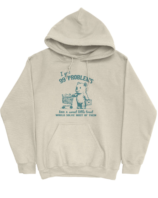 Flat lay of a sand beige hoodie with a cute, funny retro bear pushing a shopping cart and the quote 'I Got 99 Problems But A Sweet Little Treat Is Solving Most Of Them'.