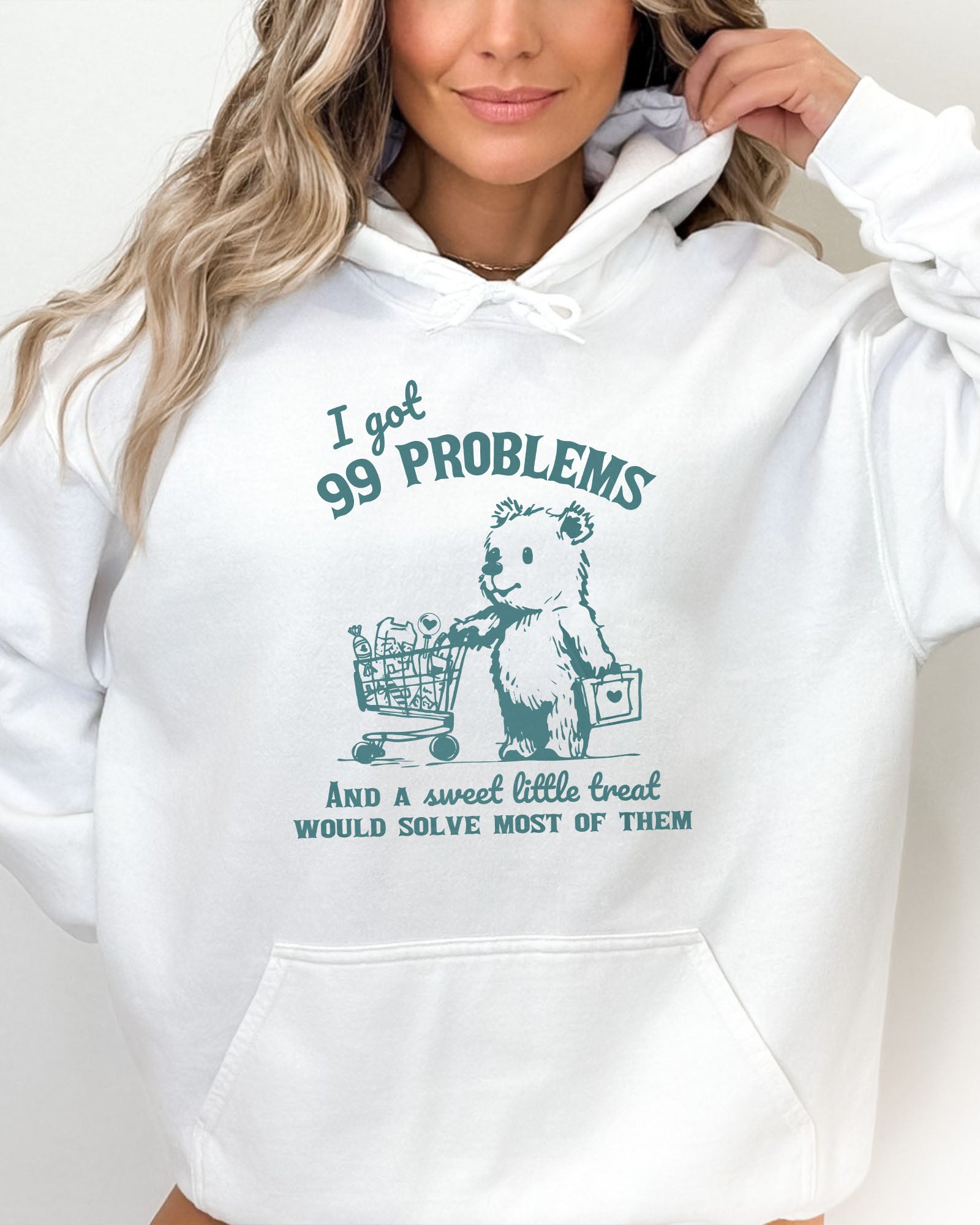 Woman wearing a white hoodie with a cute, funny retro bear pushing a shopping cart and the quote 'I Got 99 Problems But A Sweet Little Treat Is Solving Most Of Them'.