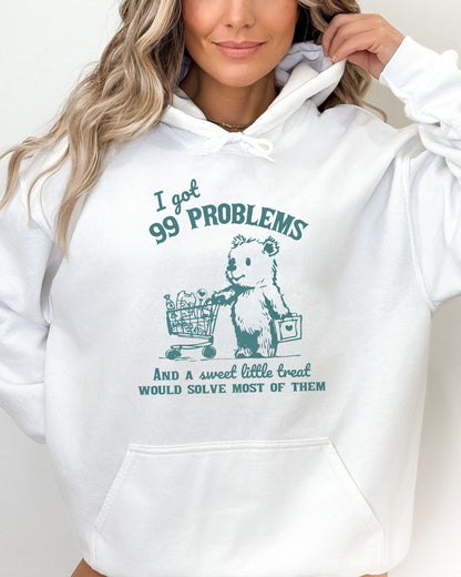 Woman wearing a white hoodie with a cute, funny retro bear pushing a shopping cart and the quote 'I Got 99 Problems But A Sweet Little Treat Is Solving Most Of Them'.
