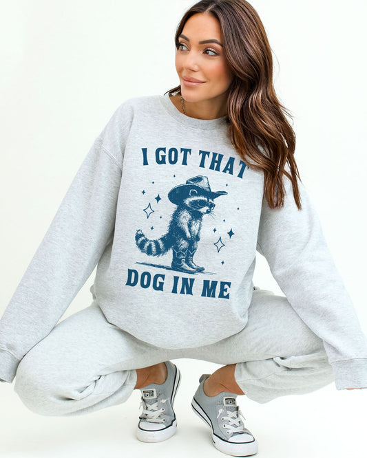 Woman wearing an ash gray  sweatshirt featuring a funny retro cowboy raccoon graphic and the quote 'I Got That Dog In Me'.