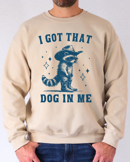Man wearing a sand beige sweatshirt featuring a funny retro cowboy raccoon graphic and the quote 'I Got That Dog In Me'.