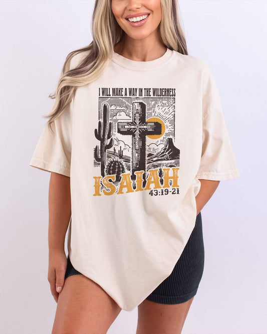 Woman wearing an ivory 'I Will Make a Way in the Wilderness – Isaiah 43:19-21' shirt with a retro graphic of a western desert and a Christian cross.