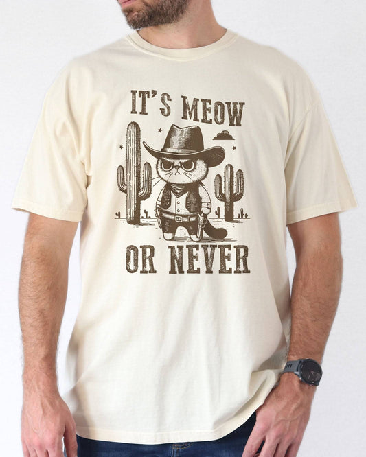 Model wearing ivory color shirt with 'It's Meow Or Never' cowboy cat graphic design