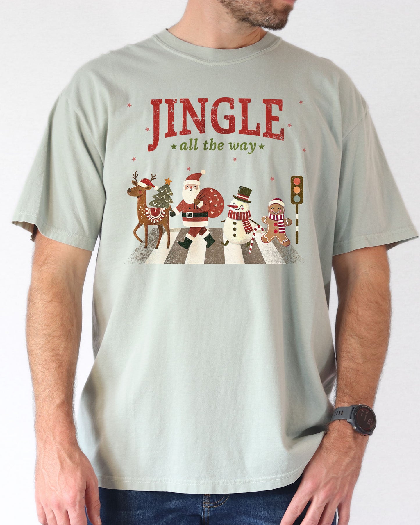 Man wearing a bay-colored 'Jingle All The Way' shirt with a retro graphic of Santa, a reindeer, snowman, and gingerbread man crossing a crosswalk.