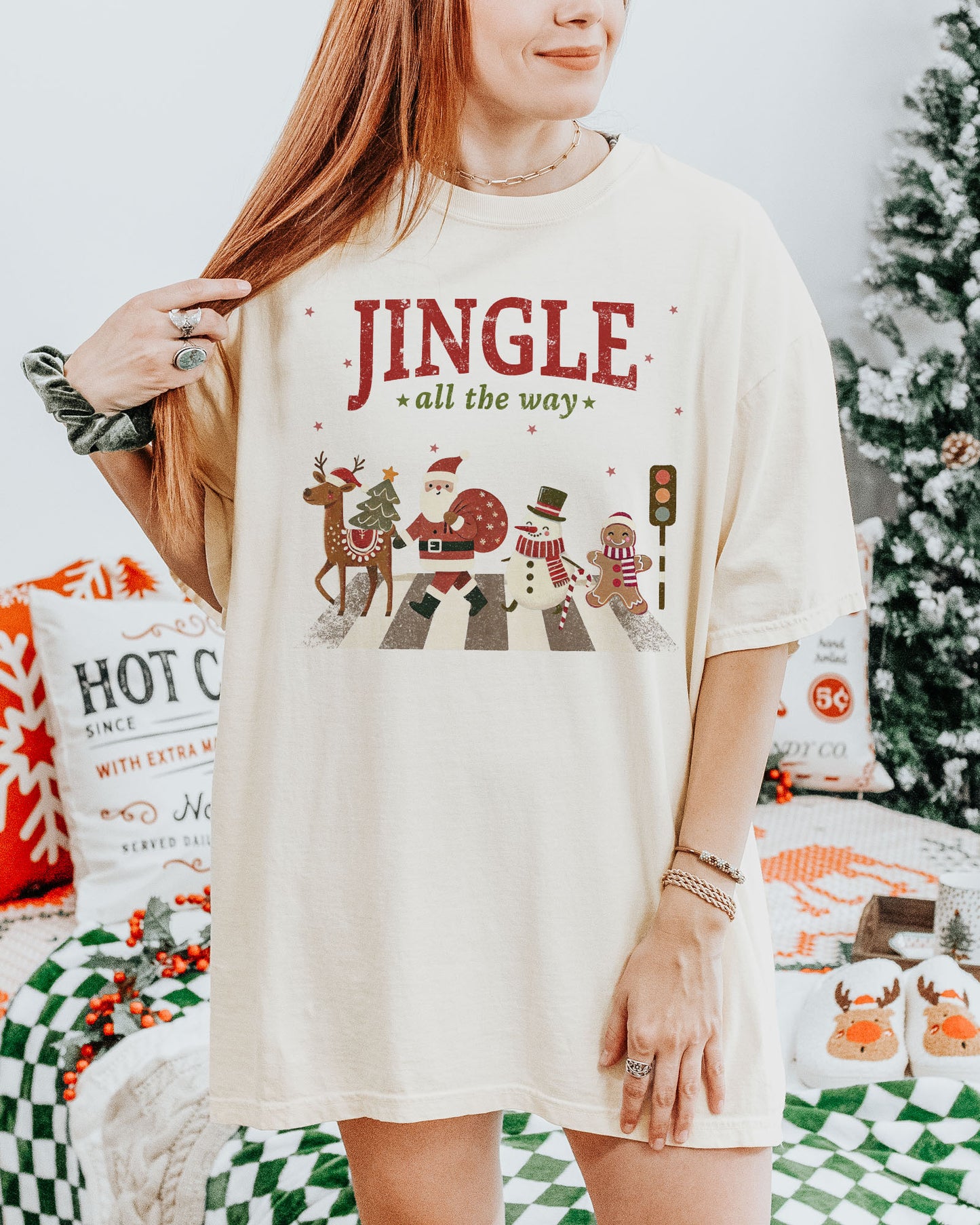 Woman wearing an ivory 'Jingle All The Way' shirt with a retro graphic of Santa, a reindeer, snowman, and gingerbread man crossing a crosswalk.