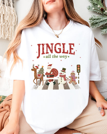 Woman wearing a white 'Jingle All The Way' shirt with a retro graphic of Santa, a reindeer, snowman, and gingerbread man crossing a crosswalk.