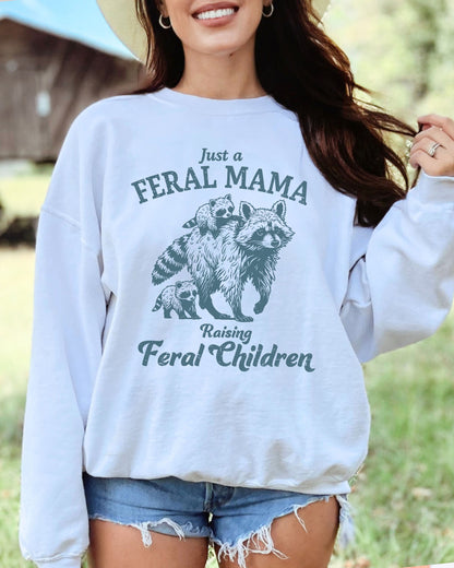 Model wearing white color sweatshirt with 'Just A Feral Mama Raising Feral Children' raccoons graphic design