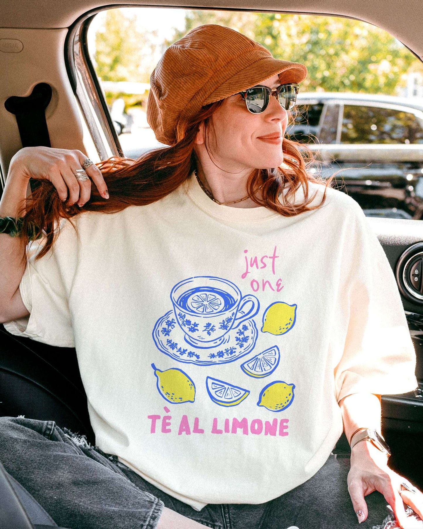 Woman wearing an ivory “Just One Té Al Limone” shirt with a retro graphic of a steaming cup of lemon tea and fresh lemons.