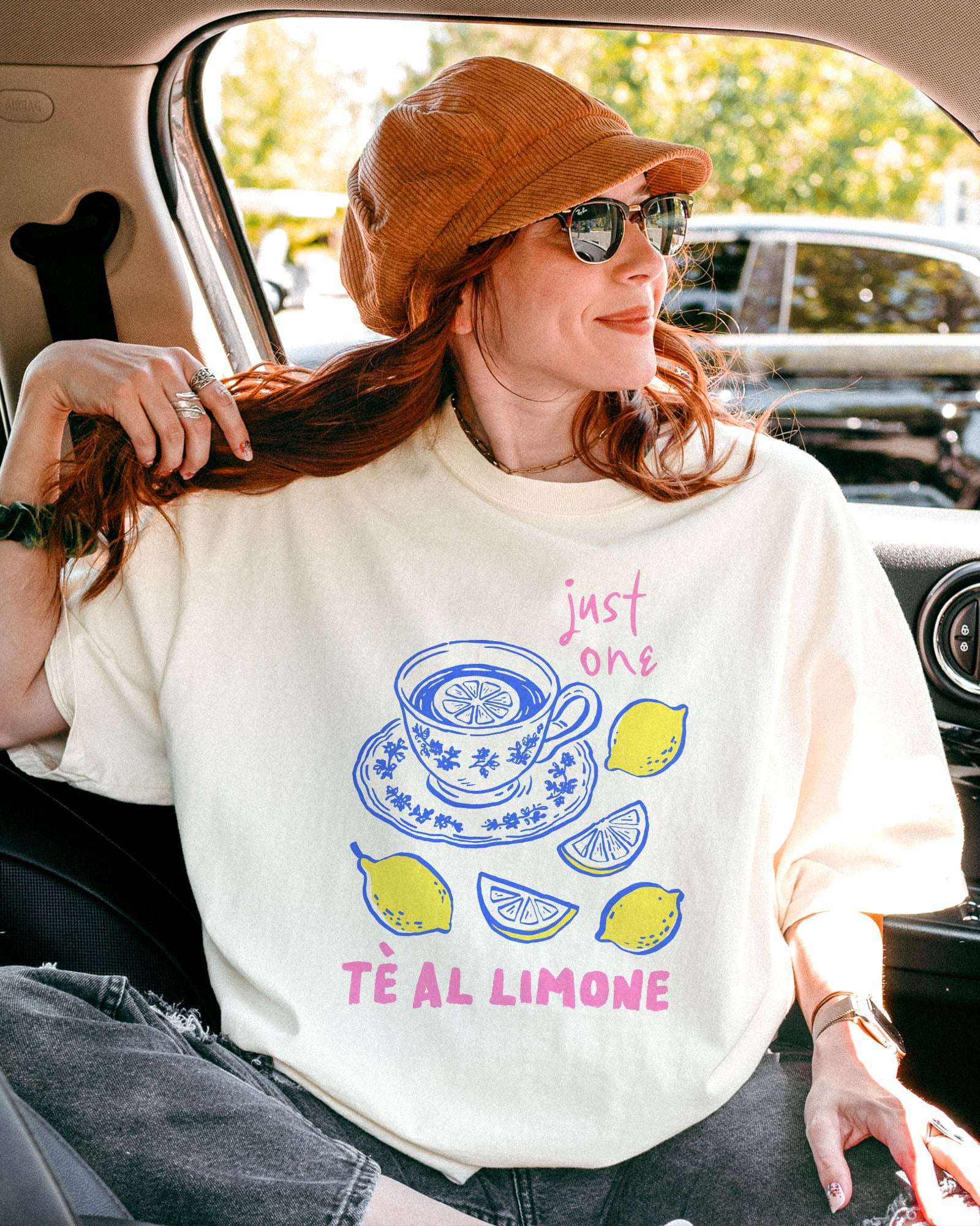 Woman wearing an ivory “Just One Té Al Limone” shirt with a retro graphic of a steaming cup of lemon tea and fresh lemons.