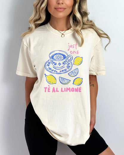 Woman wearing an ivory “Just One Té Al Limone” shirt with a retro graphic of a steaming cup of lemon tea and fresh lemons.