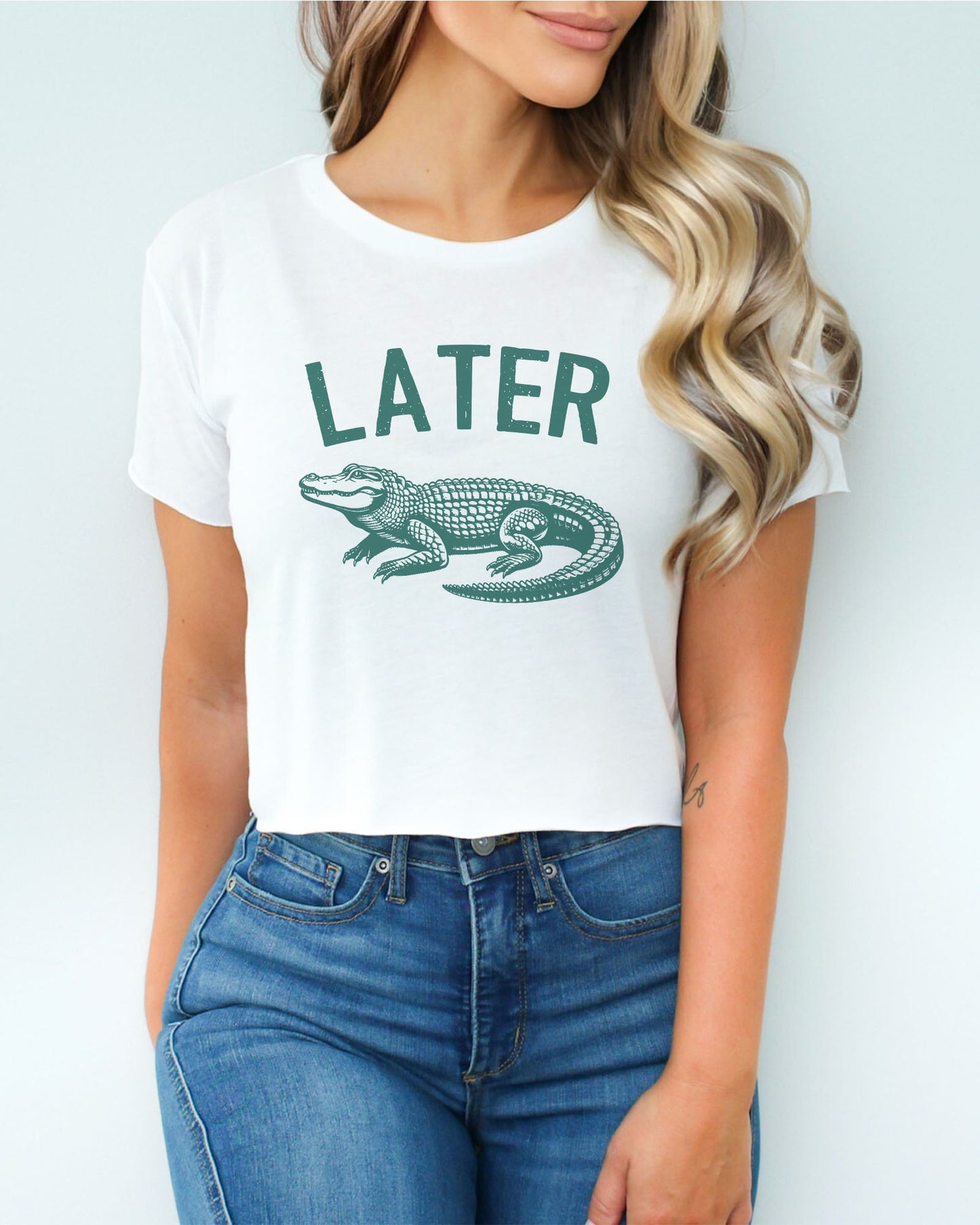 Woman wearing a white-colored 'Later Gator' crop top featuring a funny retro alligator graphic.