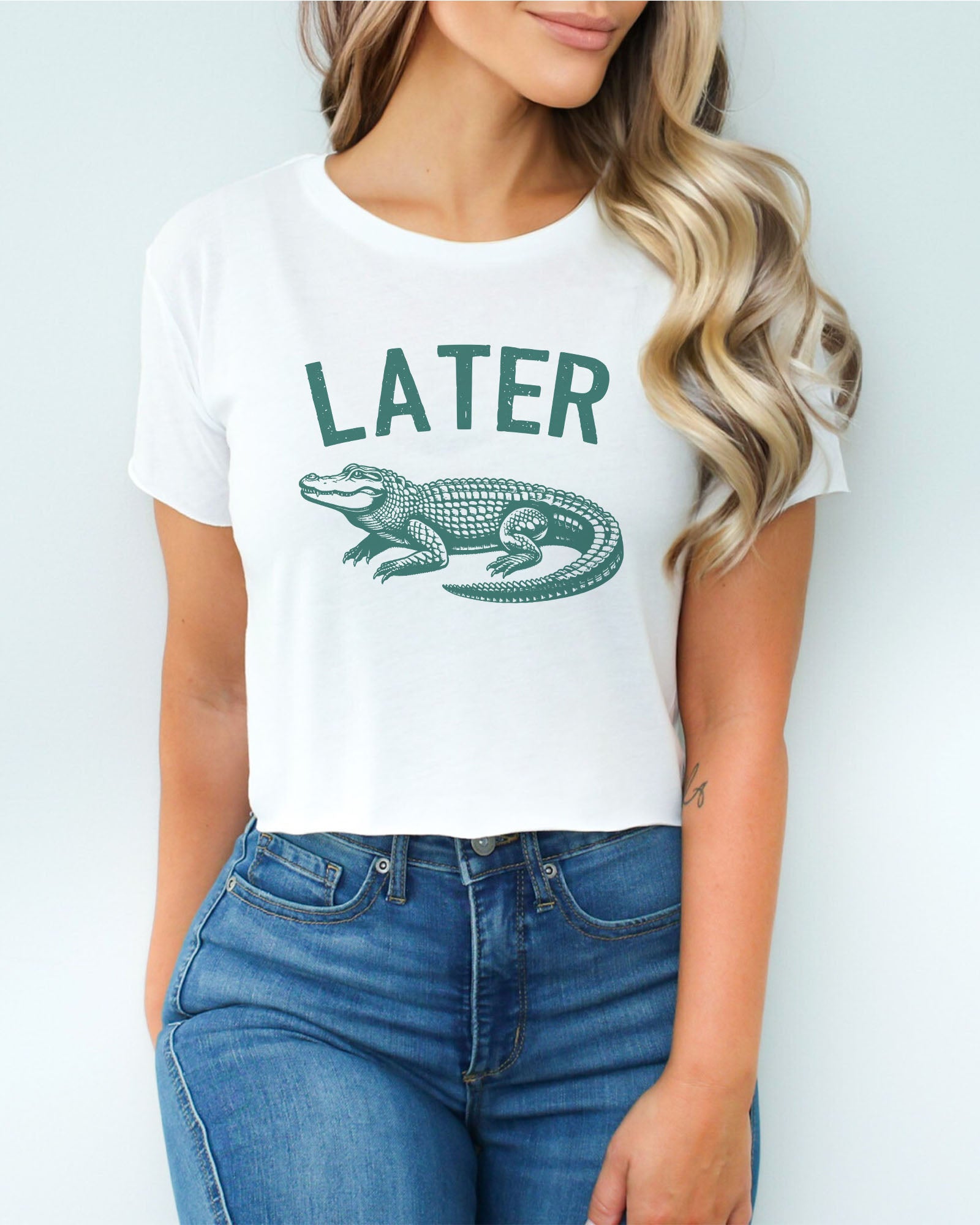 Woman wearing a white-colored 'Later Gator' crop top featuring a funny retro alligator graphic.