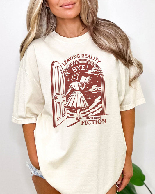 Woman wearing an ivory 'Leaving Reality Entering Fiction' shirt with a funny retro graphic of a woman reading while stepping through a door into a new universe.