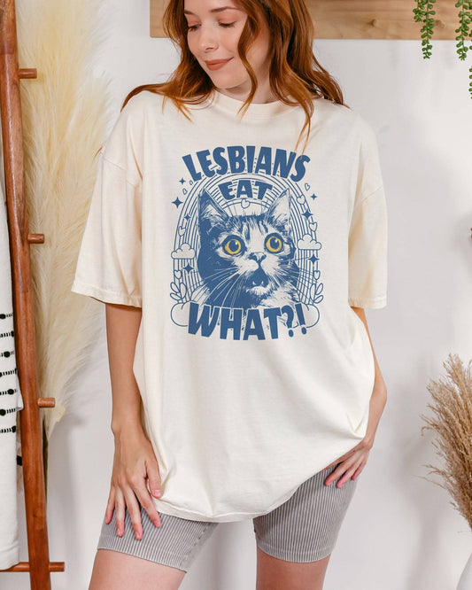 Woman wearing "Lesbians Eat What?!" shirt in ivory color with a funny retro graphic of a shocked cat.