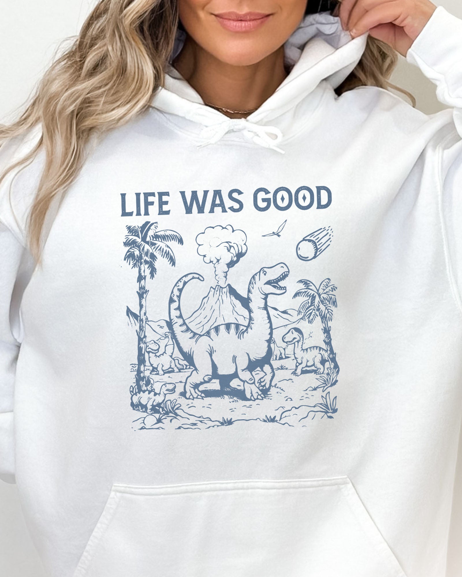 Close-up of a white hoodie featuring a retro-style graphic of dinosaurs going extinct from an asteroid, with the text 'Life Was Good'.