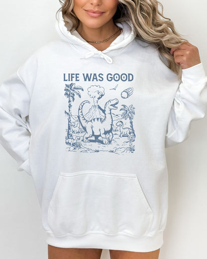 Woman wearing a white hoodie featuring a retro-style graphic of dinosaurs going extinct from an asteroid, with the text 'Life Was Good'.