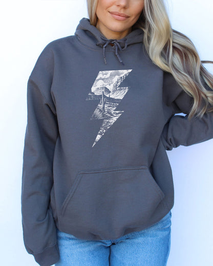 Woman wearing a charcoal gray hoodie featuring a retro vintage-style western desert scenery lightning bolt graphic.