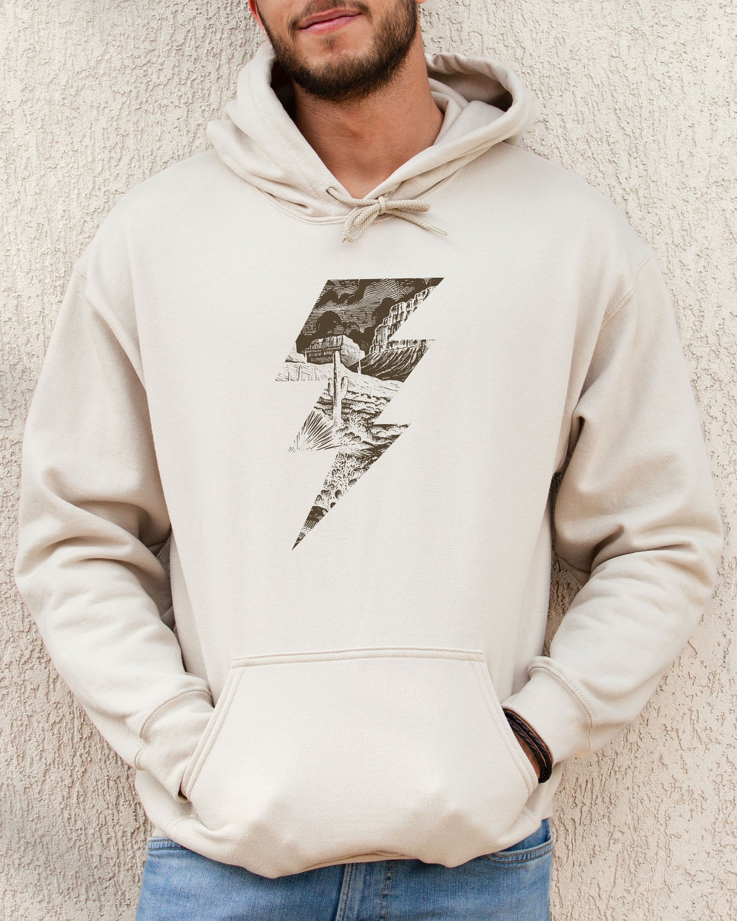 Man wearing a sand beige hoodie featuring a retro vintage-style western desert scenery lightning bolt graphic.