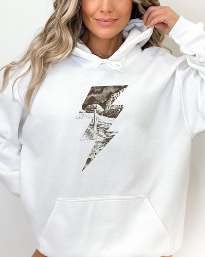 Woman wearing a white hoodie featuring a retro vintage-style western desert scenery lightning bolt graphic.