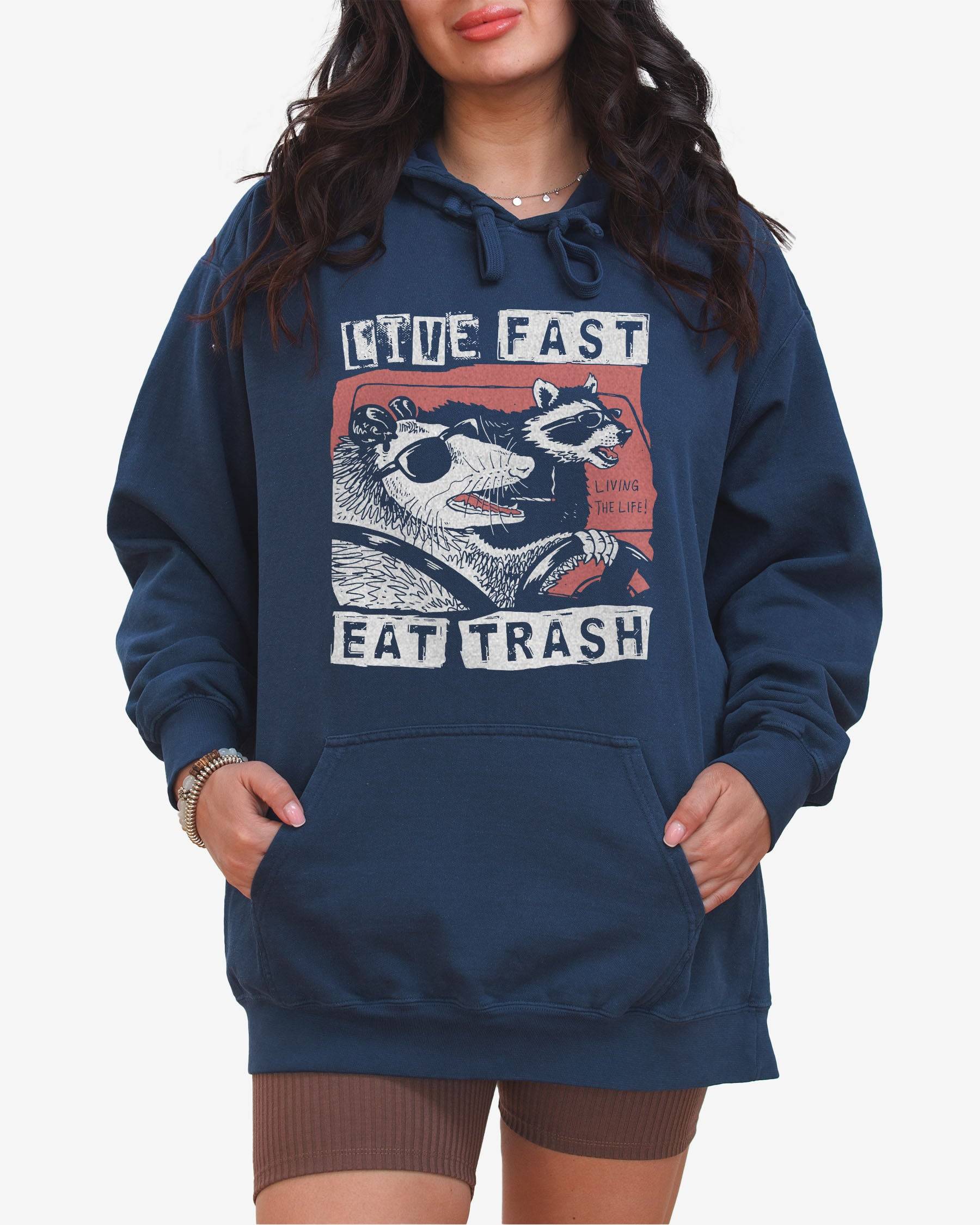 Woman wearing true navy 'Live Fast Eat Trash' hoodie with a funny retro graphic of two raccoons driving a car.