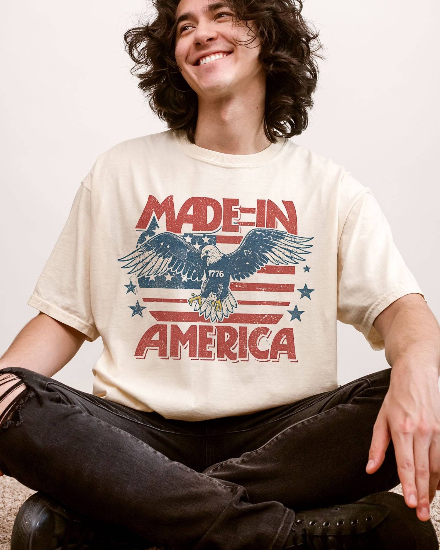Man wearing "Made In America 1776" shirt in ivory color with retro graphic of a hawk in USA red-white-and-blue colors.