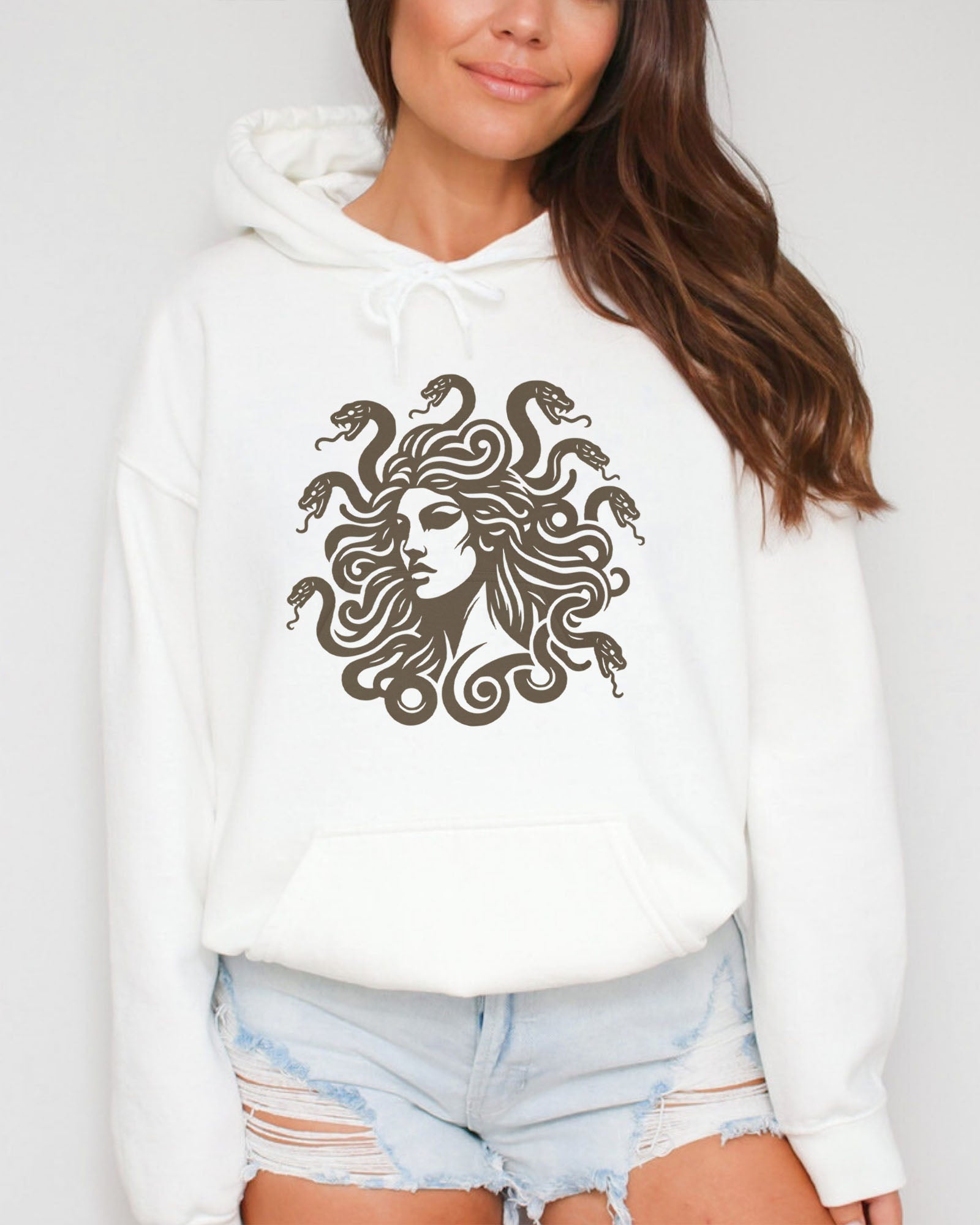 Woman wearing a white hoodie featuring a vintage-style Medusa graphic with snake hair.