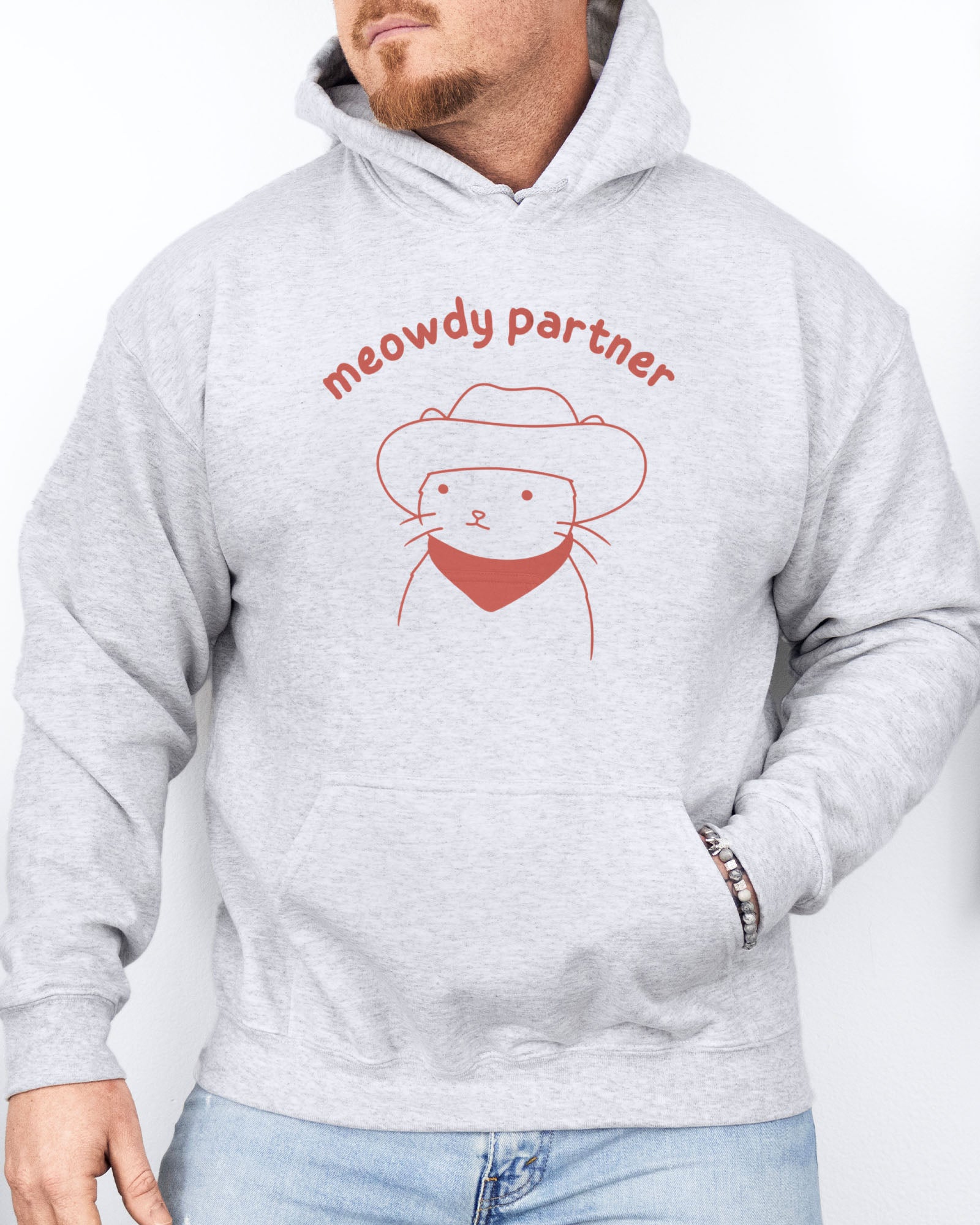 Man wearing an ash gray hoodie featuring a funny retro cowboy cat line-art graphic with the quote 'Meowdy Partner'.