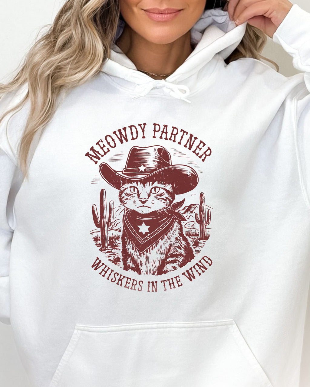 Close-up of a white hoodie with a funny retro cowboy cat graphic and the text 'Meowdy Partner, Whiskers in the Wind' in a western-style design.