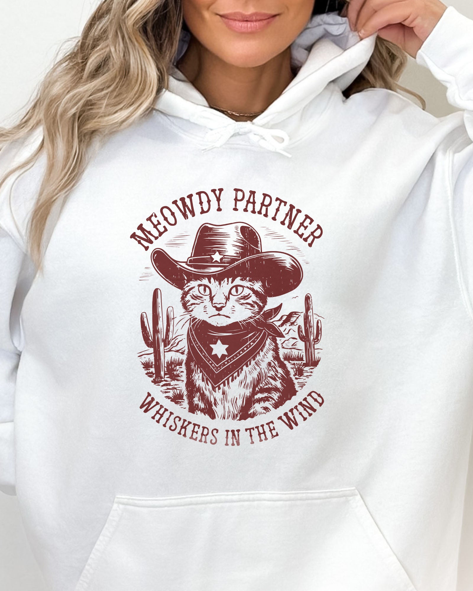 Close-up of a white hoodie with a funny retro cowboy cat graphic and the text 'Meowdy Partner, Whiskers in the Wind' in a western-style design.