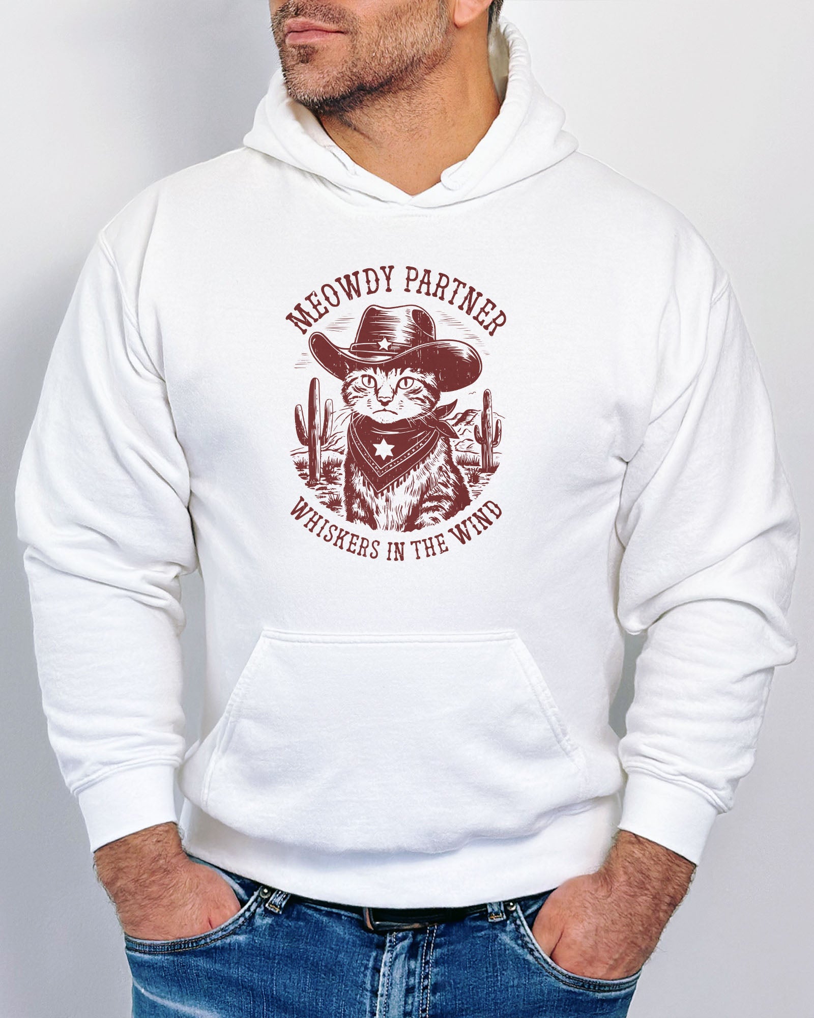 Man wearing a white hoodie with a funny retro cowboy cat graphic and the text 'Meowdy Partner, Whiskers in the Wind' in a western-style design.