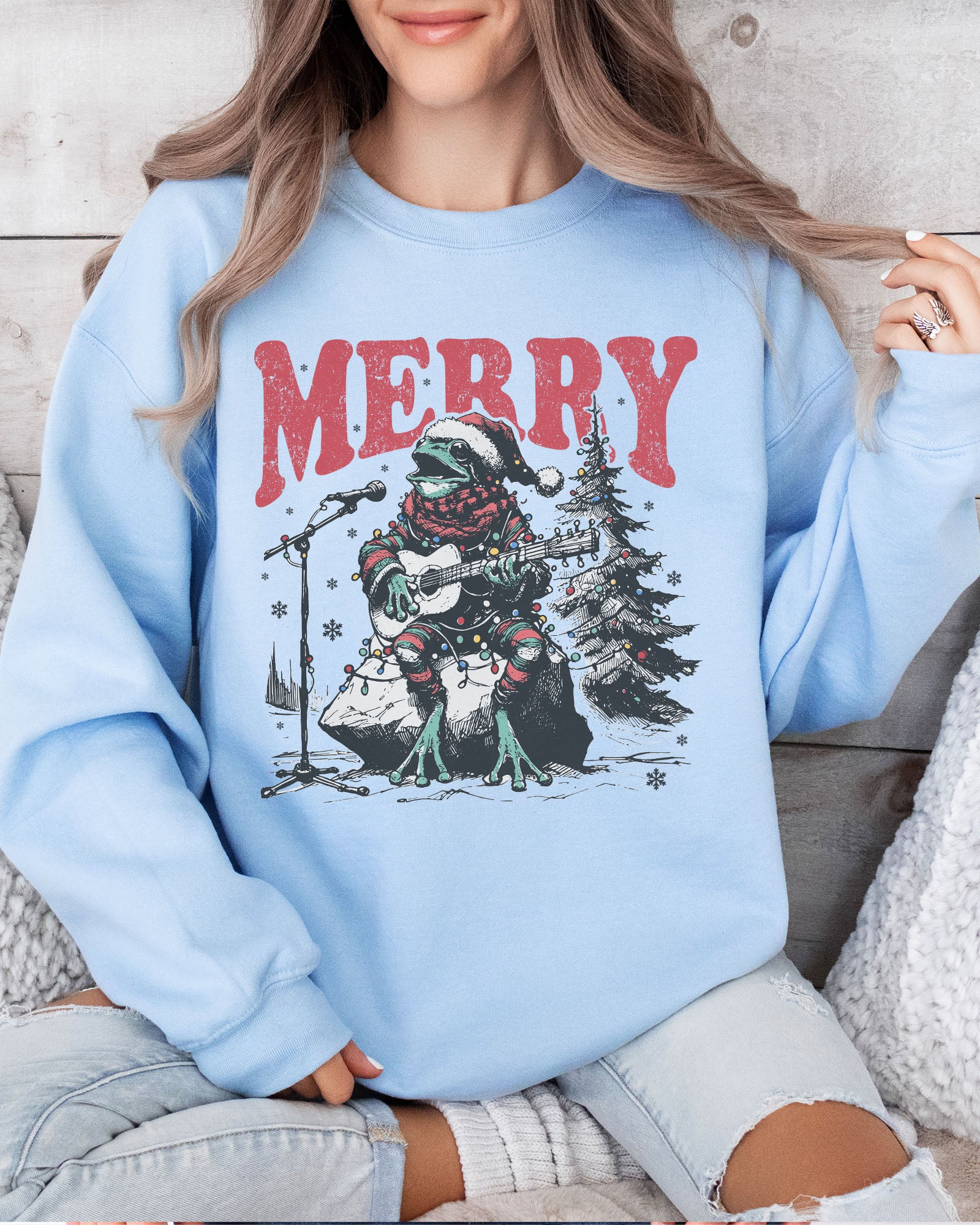 Model wearing light blue color sweatshirt with 'Merry Frog' graphic design
