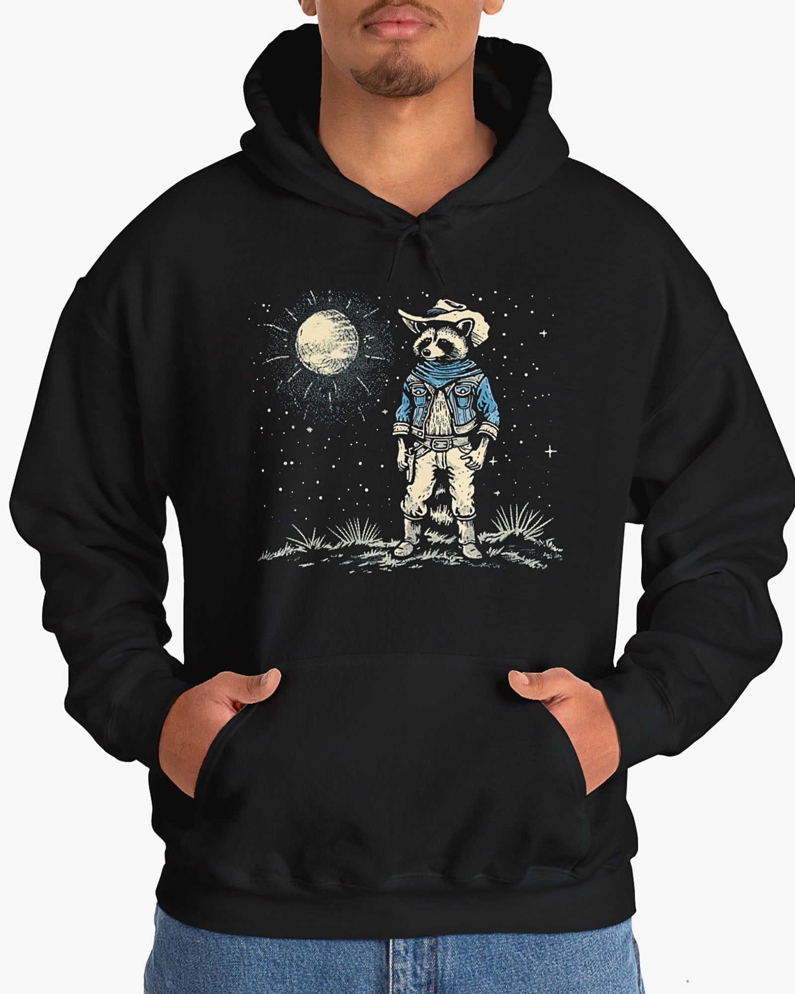 Man wearing a black hoodie featuring a retro Wild West graphic of a cowboy raccoon standing under a moonlit desert sky. The vintage-style design pops against the dark fabric.
