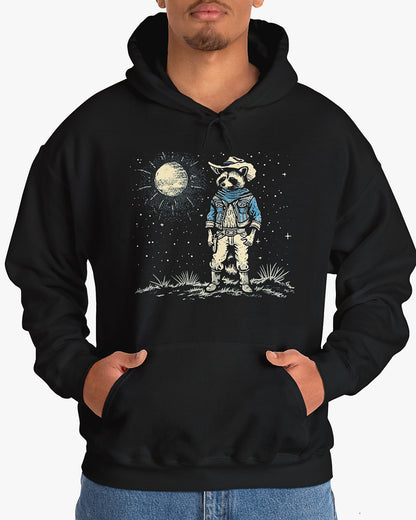 Man wearing a black hoodie featuring a retro Wild West graphic of a cowboy raccoon standing under a moonlit desert sky. The vintage-style design pops against the dark fabric.