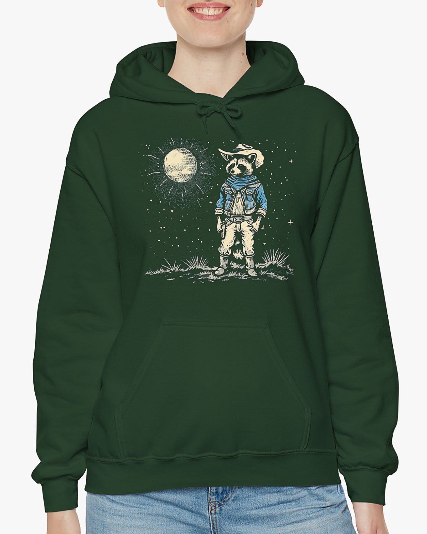 Woman wearing a forest green hoodie featuring a retro Wild West graphic of a cowboy raccoon standing under a moonlit desert sky. The vintage-style design pops against the dark fabric.