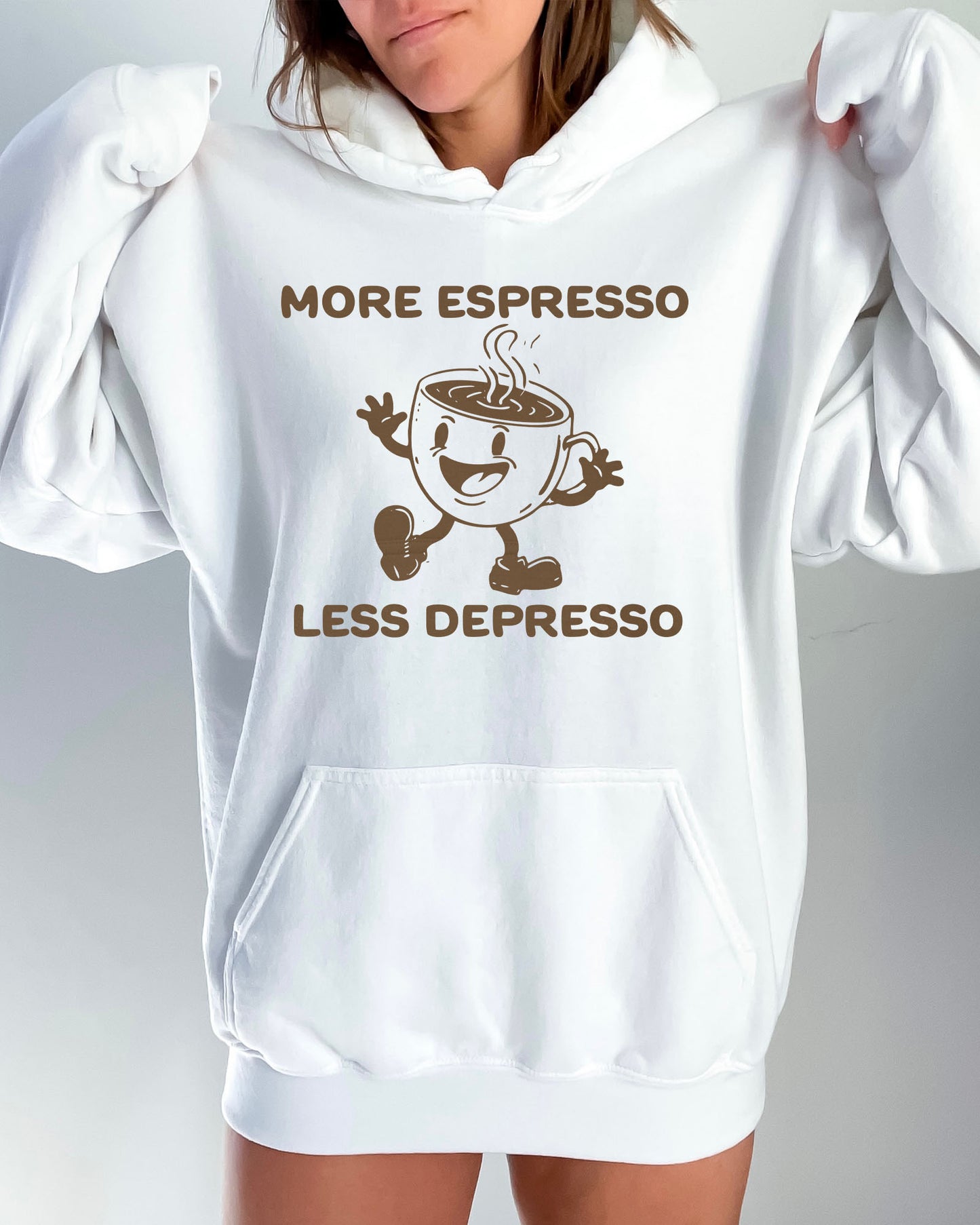 Woman wearing a white hoodie with a funny retro-style coffee mug character and the quote 'More Espresso Less Depresso' in bold lettering.
