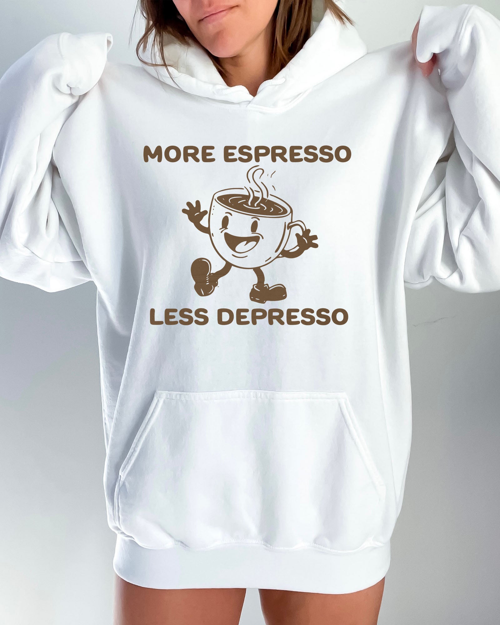 Woman wearing a white hoodie with a funny retro-style coffee mug character and the quote 'More Espresso Less Depresso' in bold lettering.