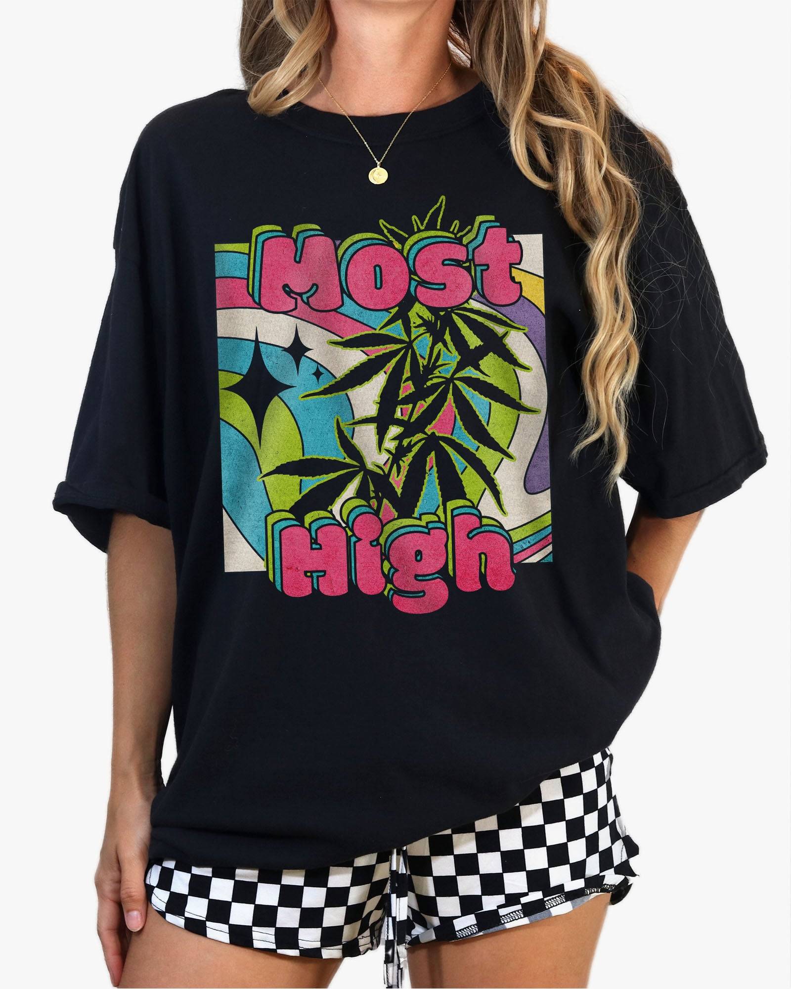 Woman  wearing a black ‘Most High’ shirt with a retro multicolor trippy collage graphic of cannabis plants.