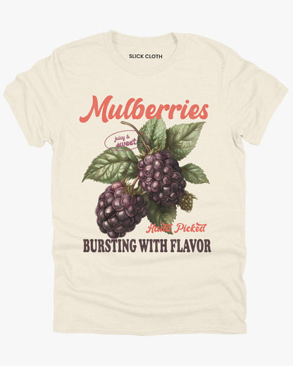 Flat lay of a natural-colored t-shirt featuring a retro fruit graphic with the quote 'Mulberries - Bursting With Flavor.'