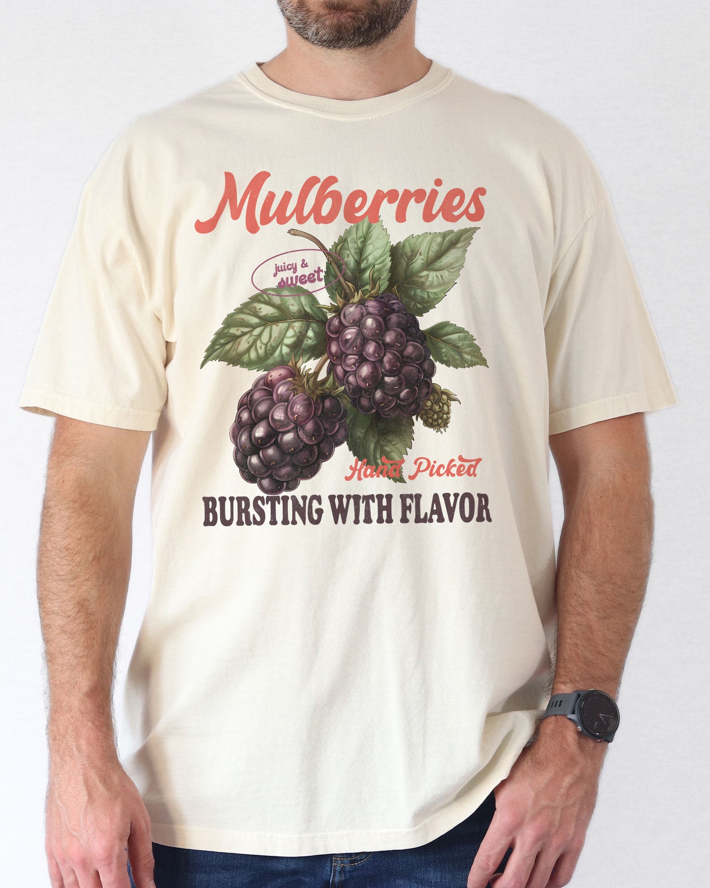 Man wearing a natural t-shirt featuring a retro fruit graphic with the quote 'Mulberries - Bursting With Flavor.'
