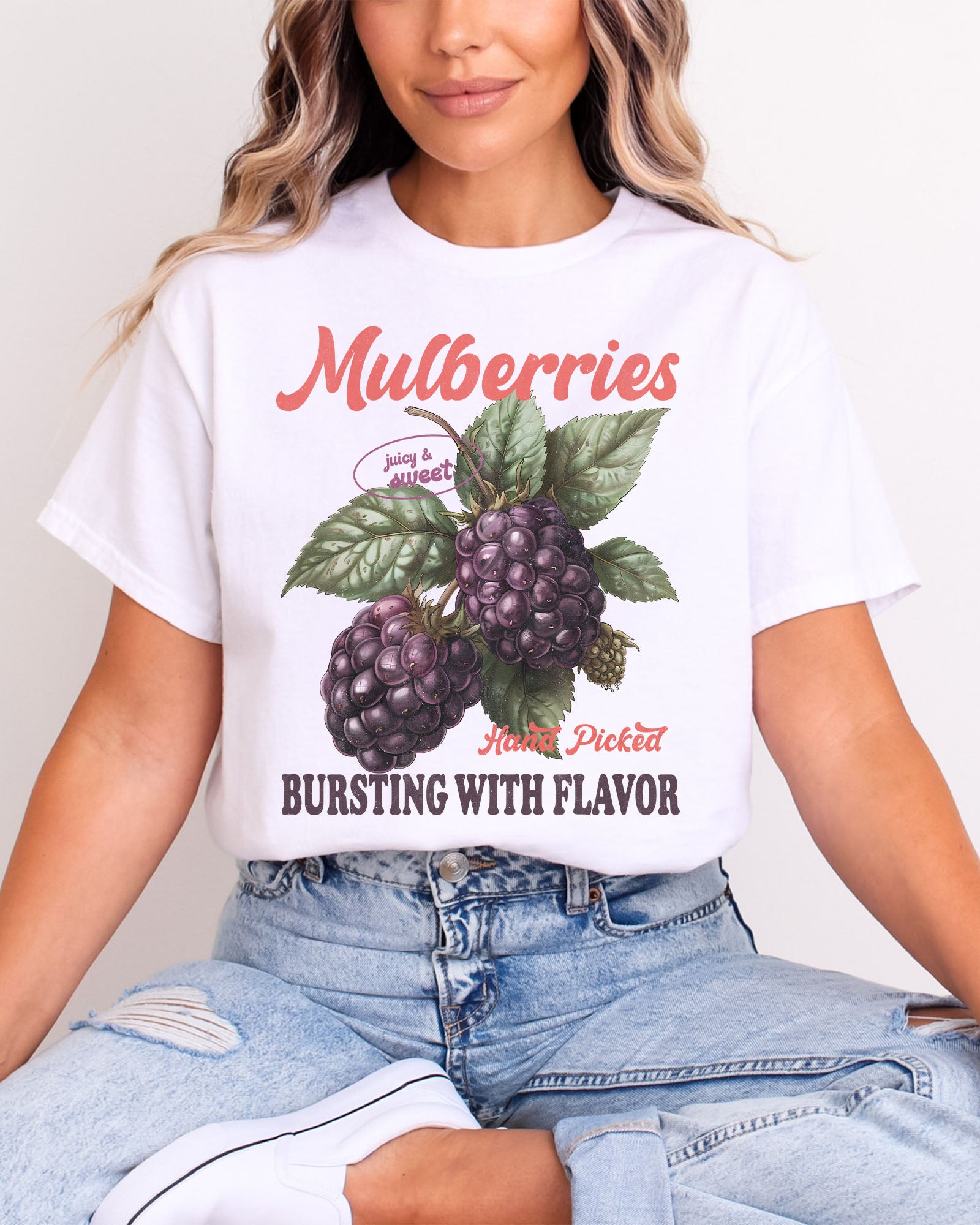 Woman wearing a white t-shirt featuring a retro fruit graphic with the quote 'Mulberries - Bursting With Flavor.'