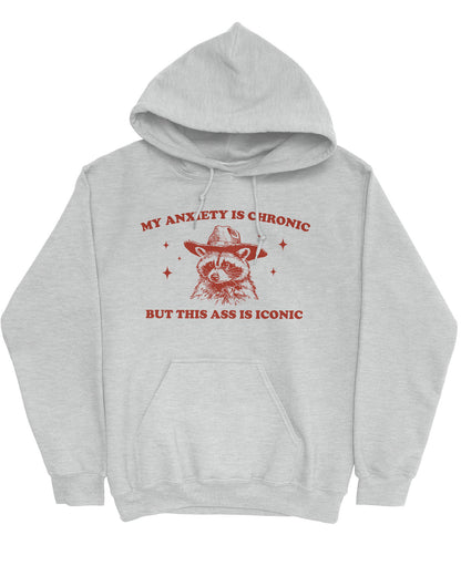 Flat lay of an ash gray 'My Anxiety Is Chronic But This Ass Is Iconic' hoodie featuring a funny retro cowboy raccoon graphic.