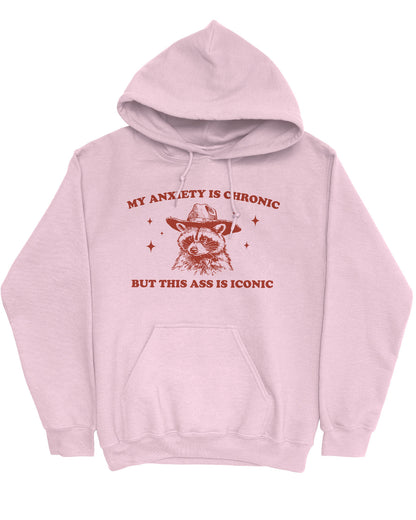 Flat lay of a light pink 'My Anxiety Is Chronic But This Ass Is Iconic' hoodie featuring a funny retro cowboy raccoon graphic.