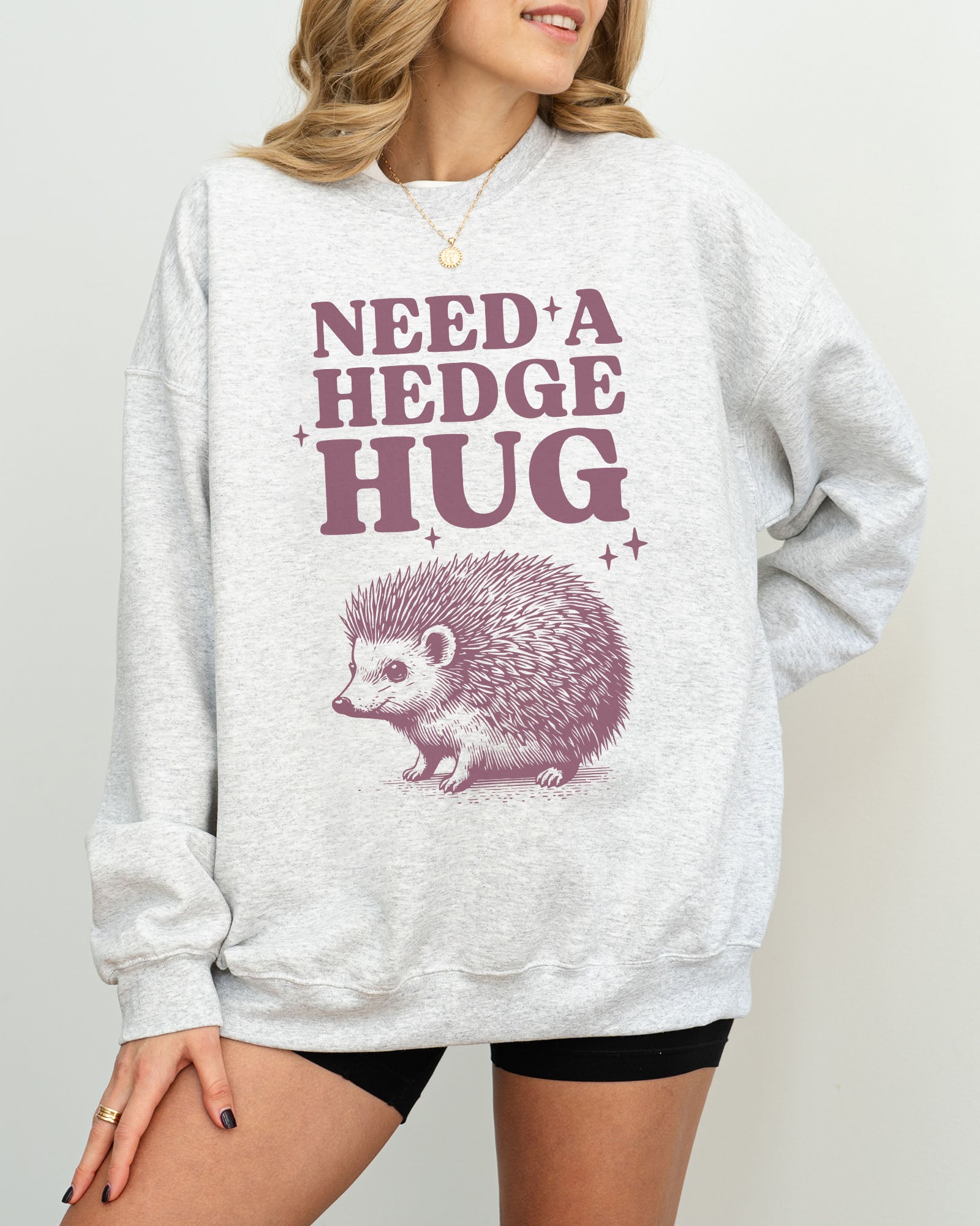 Model wearing ash color sweatshirt with 'Need A Hedge Hug' graphic design