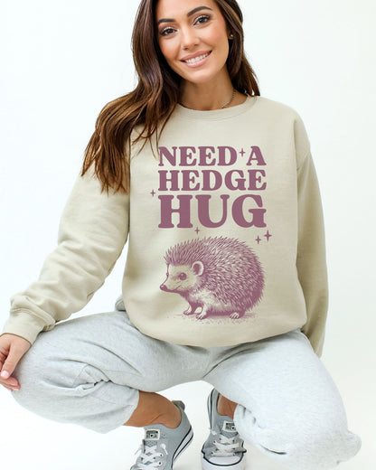 Model wearing sand color sweatshirt with 'Need A Hedge Hug' graphic design