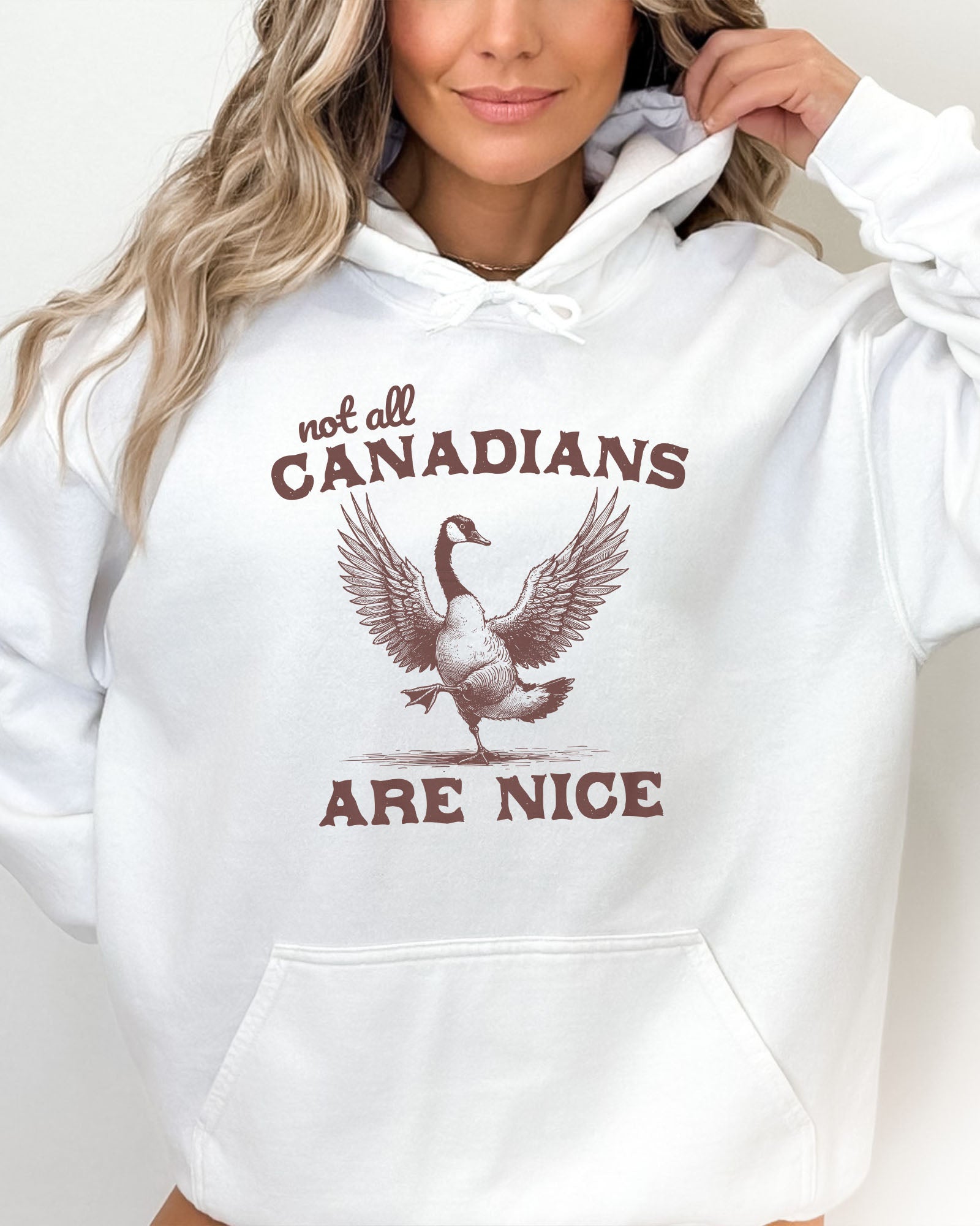 Woman wearing white-colored 'Not All Canadians Are Nice' hoodie featuring a funny canadian goose retro graphic.