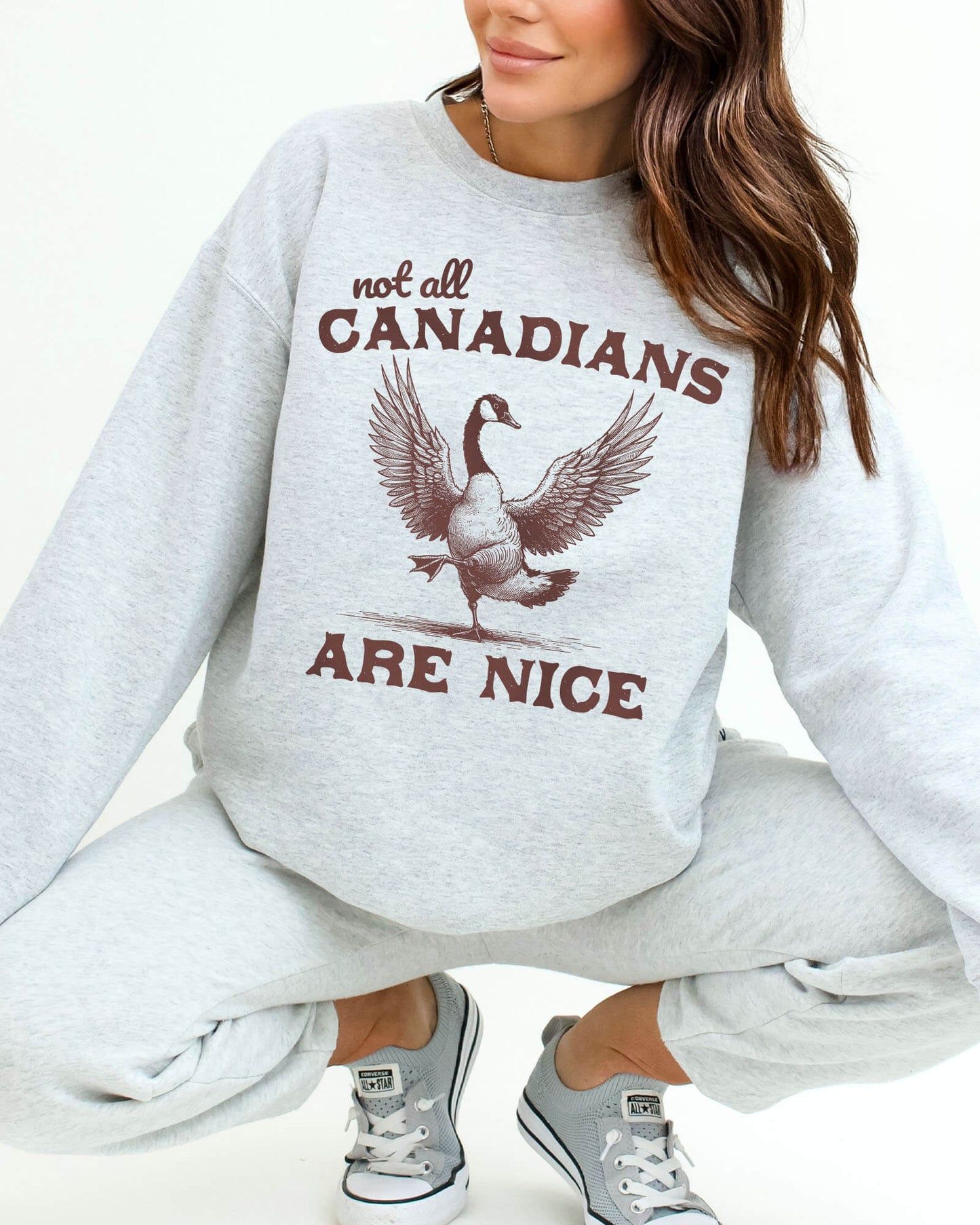 Woman wearing an ash gray sweatshirt featuring a funny retro bird graphic and the quote 'Not All Canadians Are Nice'.