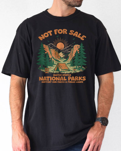 Man wearing a black 'Not For Sale - United States National Parks' shirt with a retro graphic of national park woods and a tent.
